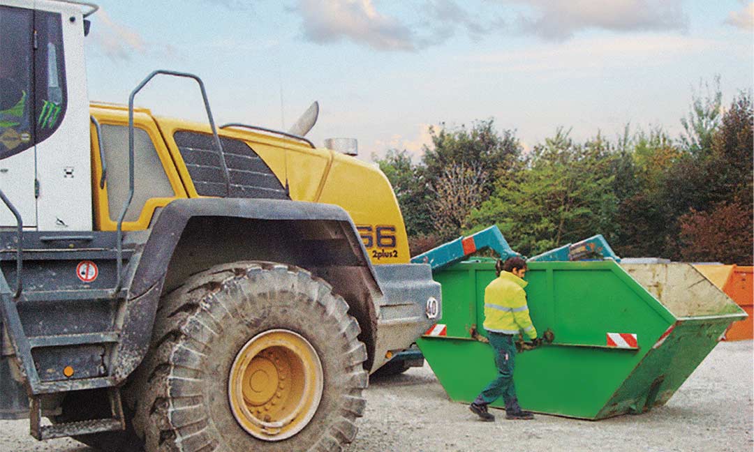 Mitarbeiter arbeitet an einer Absetzkippmulde vor einem Radlader