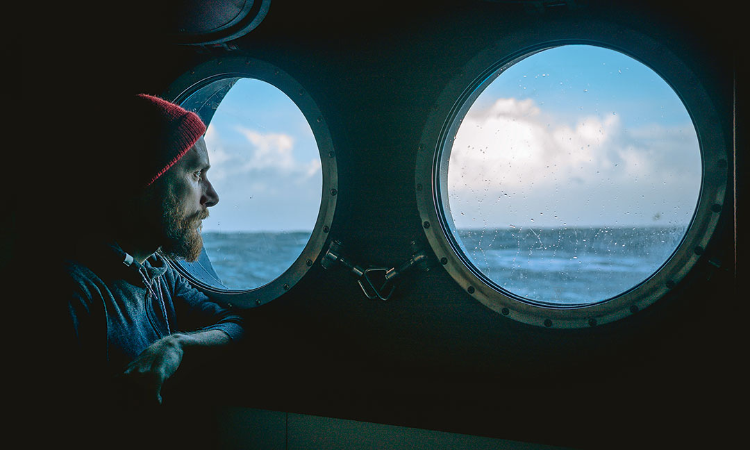 Nachdenklicher Matrose schaut aus einem Schiffsfenster raus auf die unruhige See