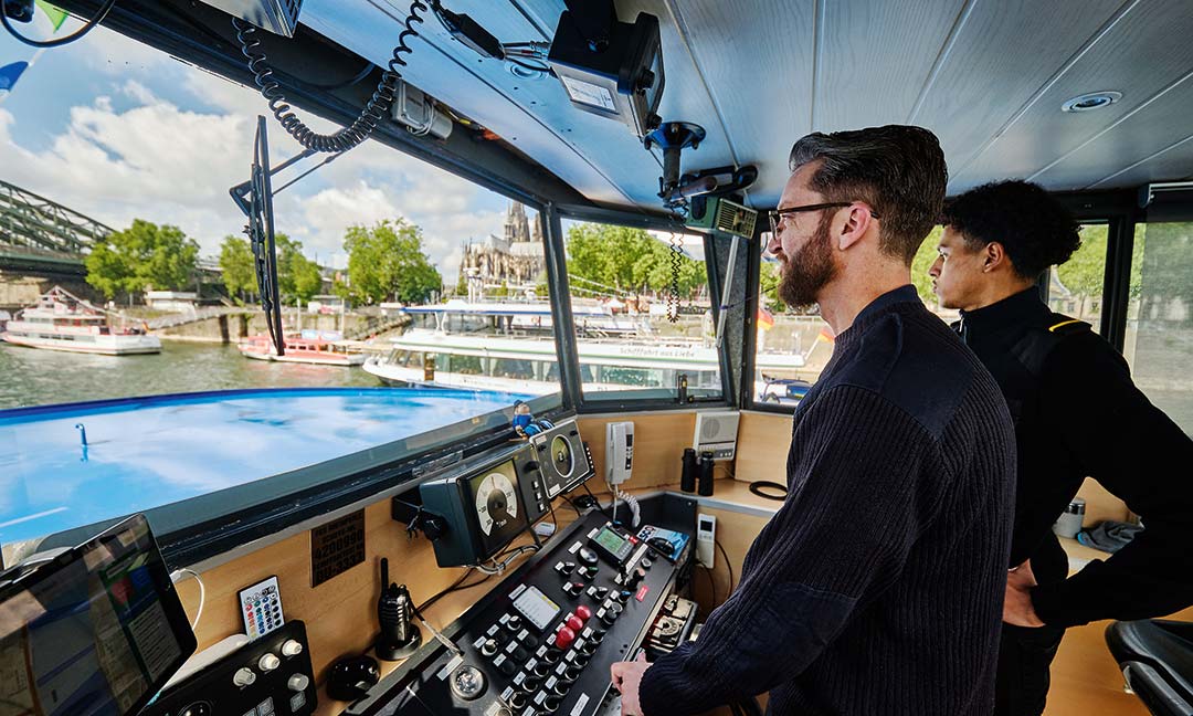 Schiffsmitarbeiter auf der Brücke eines Passagierschiffs bei der Fahrt über den Rhein