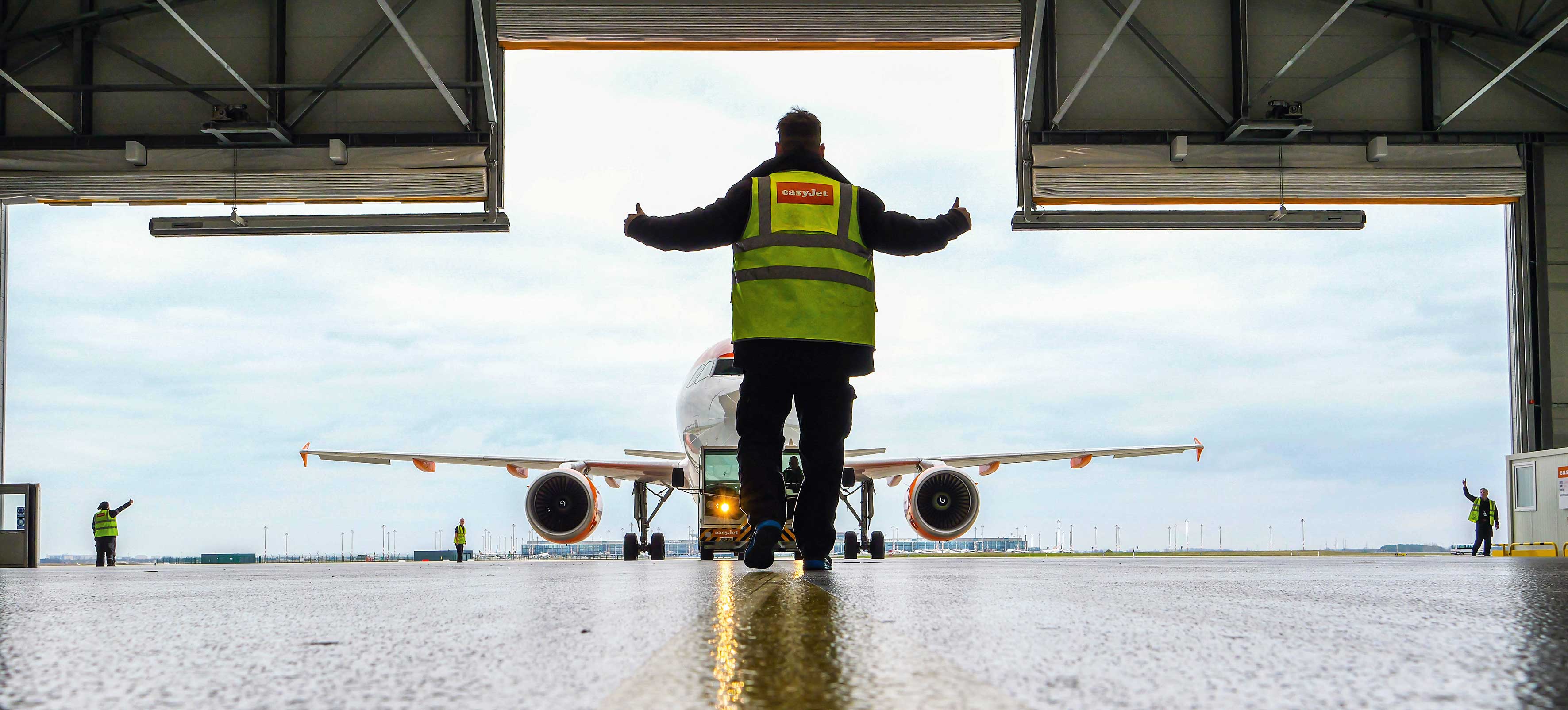 Ein Flugzeug wird in den Hangar geschleppt. Vier Mitarbeitende helfen beim Ein- und Ausweisen.
