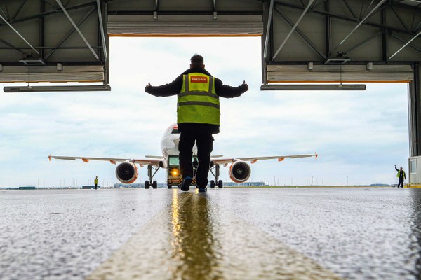 Ein Flugzeug wird in den Hangar geschleppt. Vier Mitarbeitende helfen beim Ein- und Ausweisen.