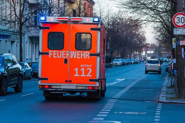 Blick von hinten auf einen Rettungswagen, der mit Blaulicht eine Straße entlangfährt.