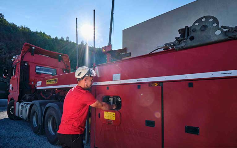 Ein Mann mit Schutzhelm steht neben einem Lastwagen und betätigt einen Hebel.