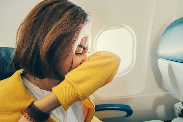 Frau in einem Passagierflugzeug niest in die Armbeuge