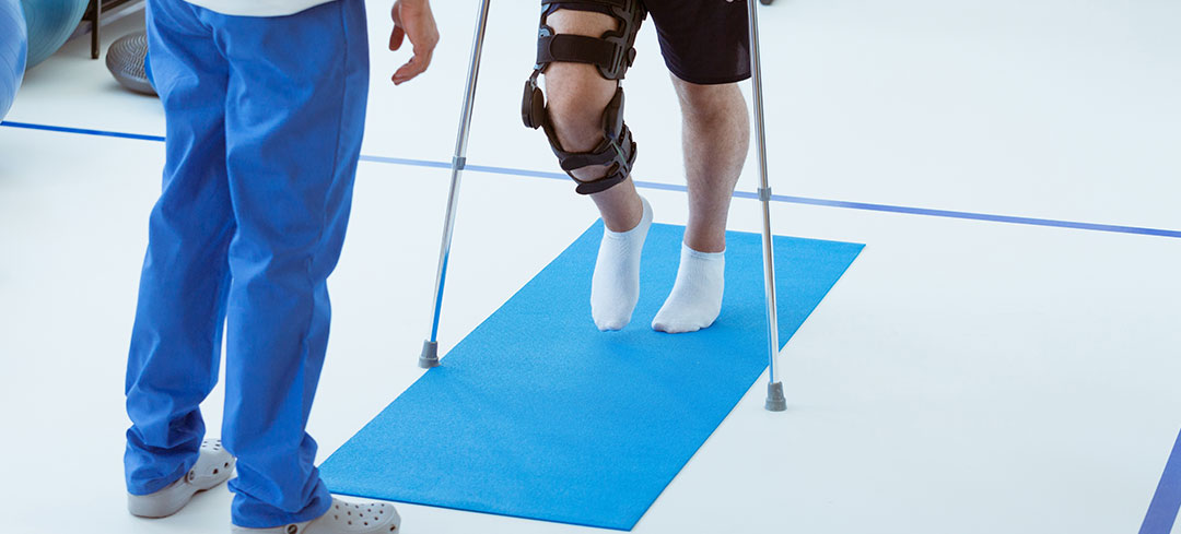 Mensch mit gestütztem Fuß auf Krücken erhält Training zur Rehabilitation