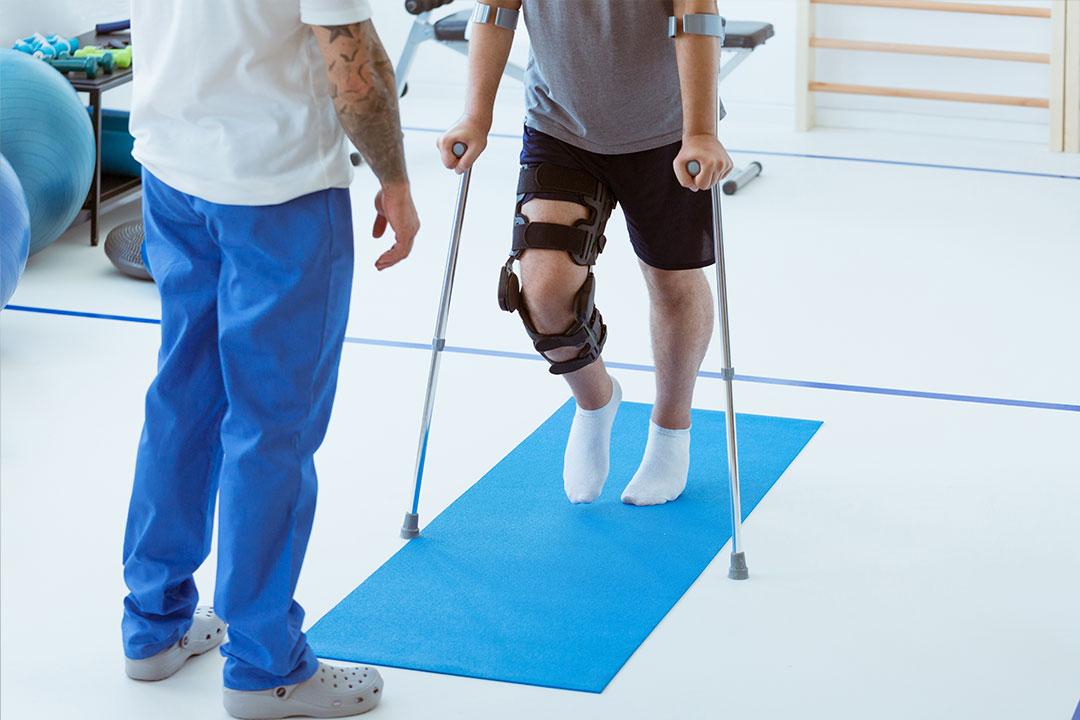 Mensch mit gestütztem Fuß auf Krücken erhält Training zur Rehabilitation