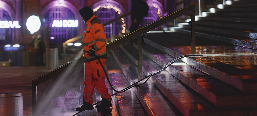 Mitarbeiter eines Entsorgungsbetriebs reinigt bei Nacht eine Treppe mit einem Schlauch