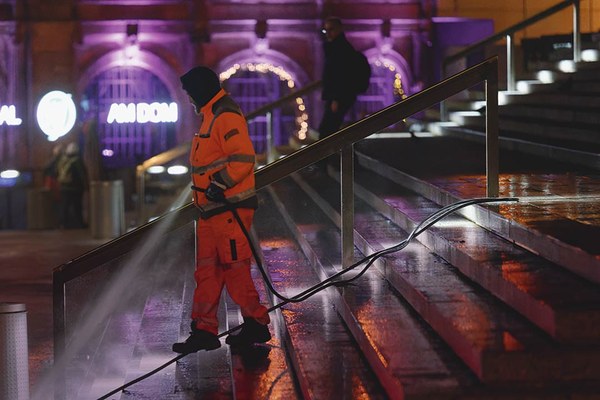 Mitarbeiter eines Entsorgungsbetriebs reinigt bei Nacht eine Treppe mit einem Schlauch