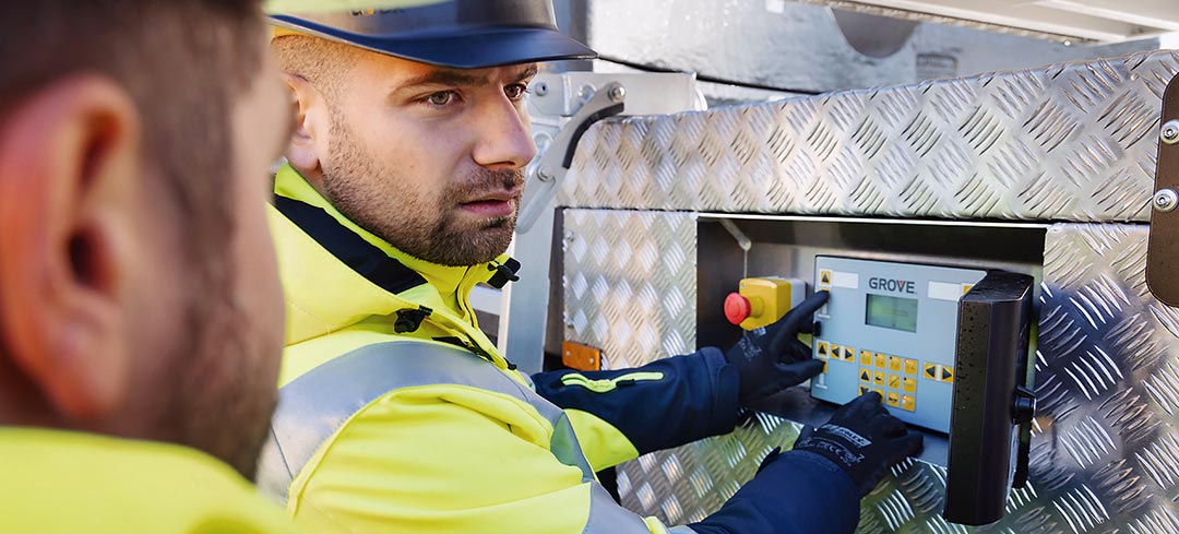 Kranprüfungen übernehmen künftig zertifizierte Sachverständige Ein Mann mit Schutzhelm drückt eine Taste auf dem Bedienteil eines Autokrans