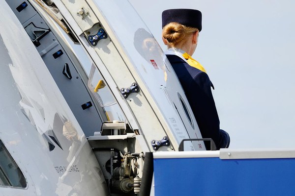Stewardess schaut aus der geöffneten Flugzeugtür in den Himmel
