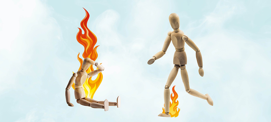 Erschöpfte, brennende Holzpuppe hält sich den Kopf – eine andere Holzpuppe springt über ein Feuer