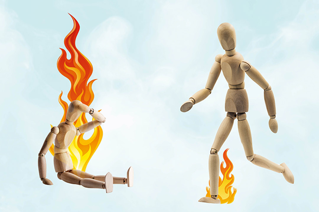 Erschöpfte, brennende Holzpuppe hält sich den Kopf – eine andere Holzpuppe springt über ein Feuer