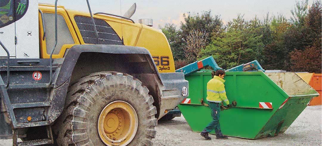 Mitarbeiter arbeitet an einer Absetzkippmulde vor einem Radlader