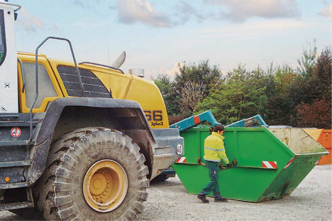 Mitarbeiter arbeitet an einer Absetzkippmulde vor einem Radlader