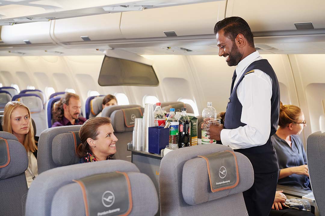 Foto eines lächelnden Flugbegleiters beim Servieren der Getränke am Trolley