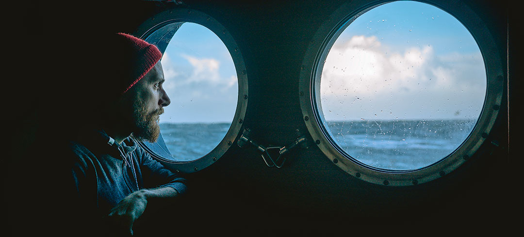 Nachdenklicher Matrose schaut aus einem Schiffsfenster raus auf die unruhige See
