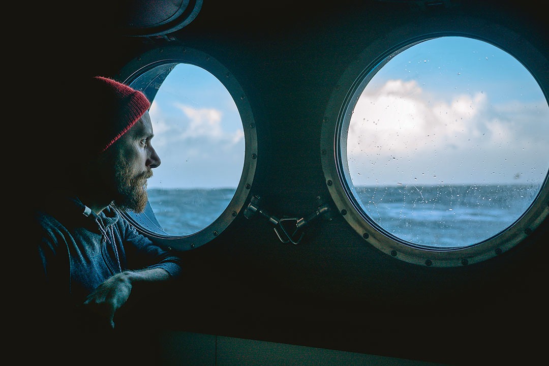 Nachdenklicher Matrose schaut aus einem Schiffsfenster raus auf die unruhige See