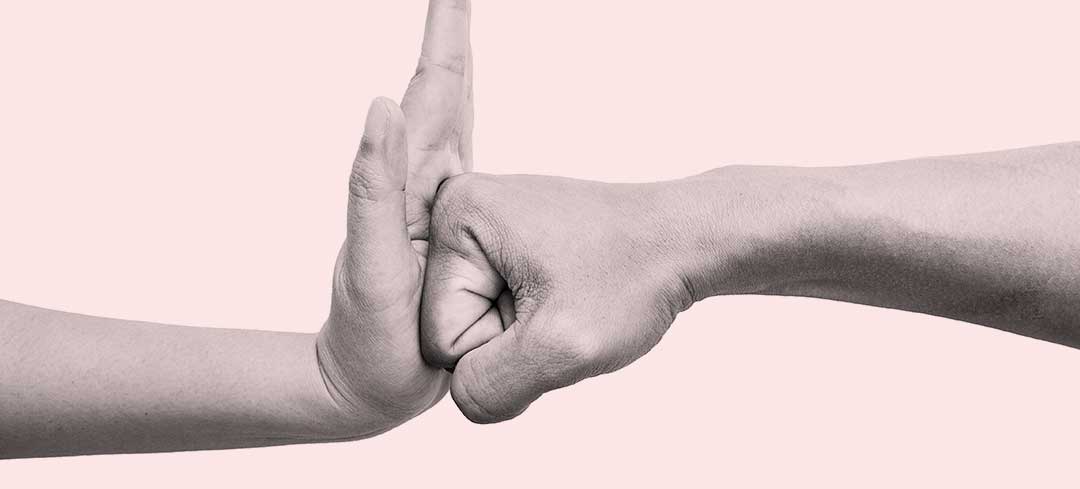 Eine flache Hand stoppt eine zur Faust geballte Hand. Eine flache Hand stoppt eine zur Faust geballte Hand.