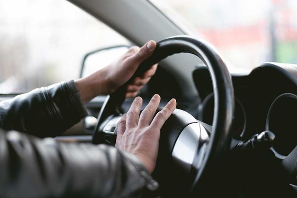 Ein Autofahrer drückt auf den Hupknopf eines Lenkrads.