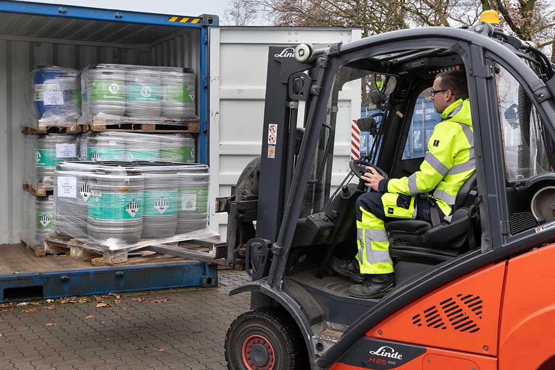 Mann in Gabelstapler belädt einen Container mit Behältern.