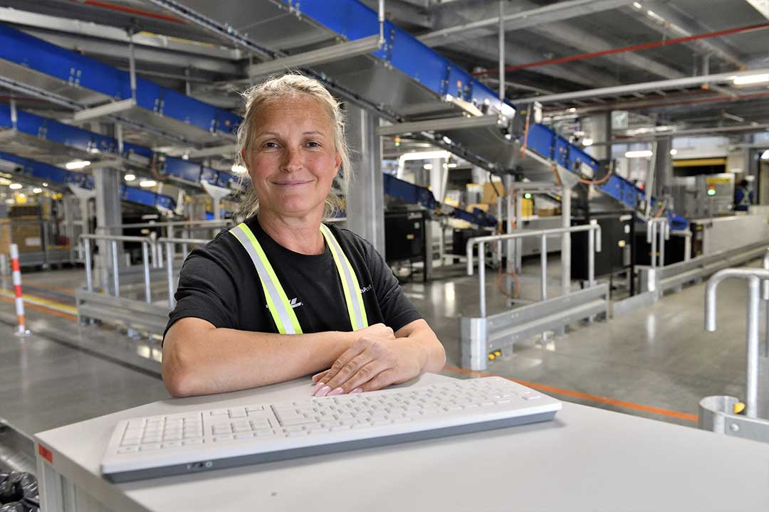 Hallenkoordinatorin Milena Miethling Eine Frau steht an einem Schreibtisch und lächelt in die Kamera. Vor ihr liegt eine Computertastatur.