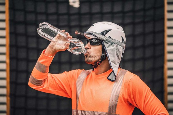 Entsorgungsmitarbeiter mit Sonnenschutzkleidung trinkt Wasser.