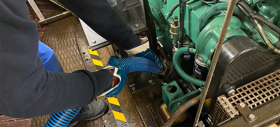 Lenzen der Bilge Zwei Hände mit Handschuhen halten einen Schlauch fest, der in den Motorraum eines Schiffes führt.