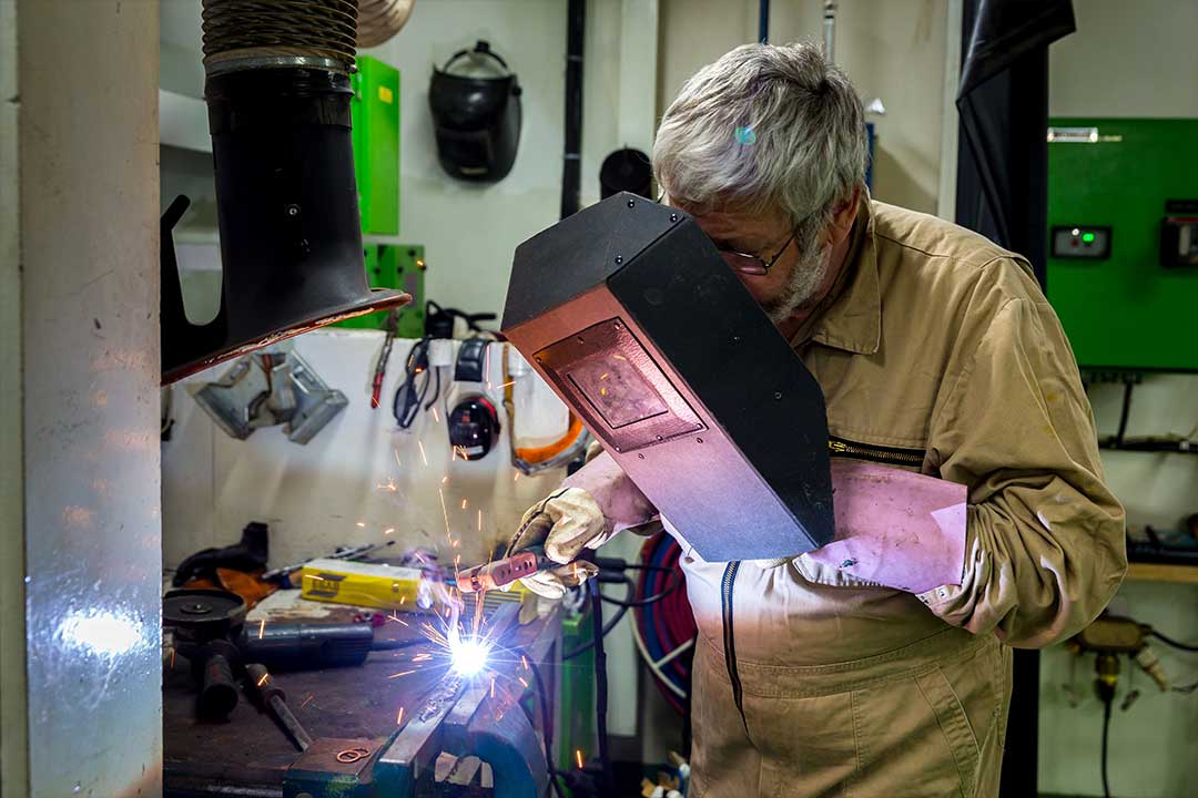 Ein Schweißer an Bord eines Schiffes bei der Arbeit. Ein Mann hält sich beim Schweißen ein Schutzschild vor die Augen.