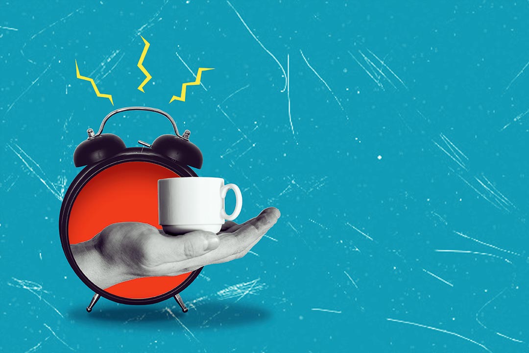 Wecker aus dem eine Hand mit einer Tasse Kaffee kommt.