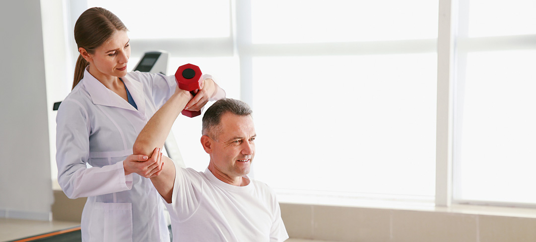 Physiotherapeutin hilft einem Patienten bei einer Rückenübung mit Hanteln