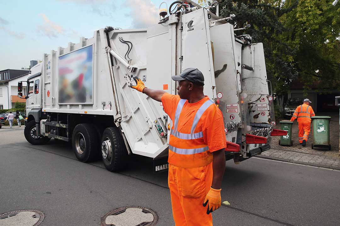 Entsorgungsmitarbeiter steht neben dem Fahrzeug und weist seinen rückwärtsfahrenden Kollegen ein