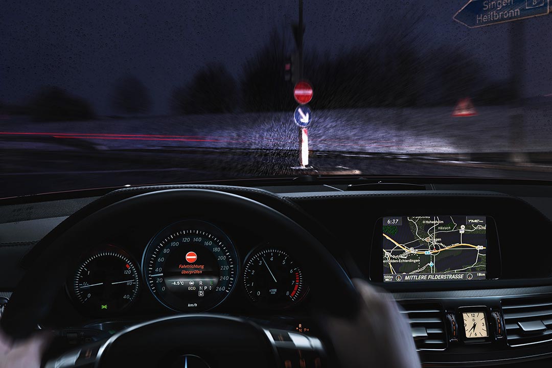 Aufnahme aus einem Pkw mit Blick auf das Cockpit und die Straße. Das Fahrerassistenztsystem warnt "Fahrtrichtung überprüfen"