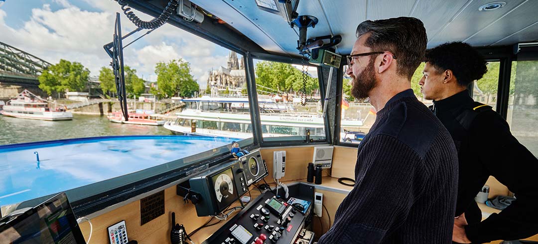 Schiffsmitarbeiter auf der Brücke eines Passagierschiffs bei der Fahrt über den Rhein