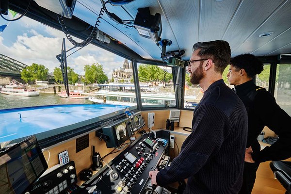 Schiffsmitarbeiter auf der Brücke eines Passagierschiffs bei der Fahrt über den Rhein