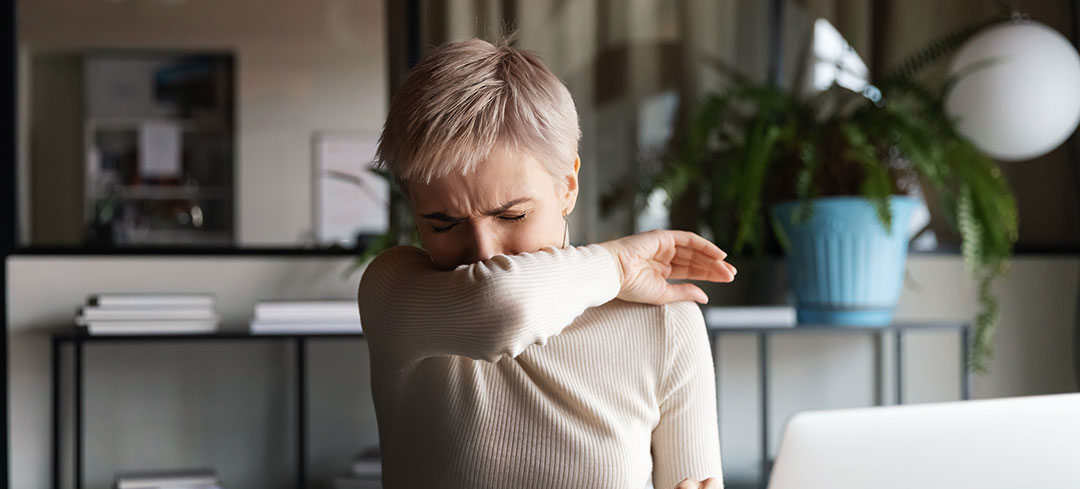 Frau im Office, die in ihre Armbeuge niest