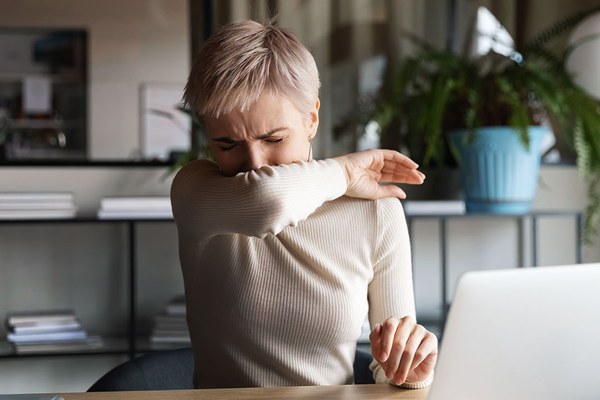 Frau im Office, die in ihre Armbeuge niest